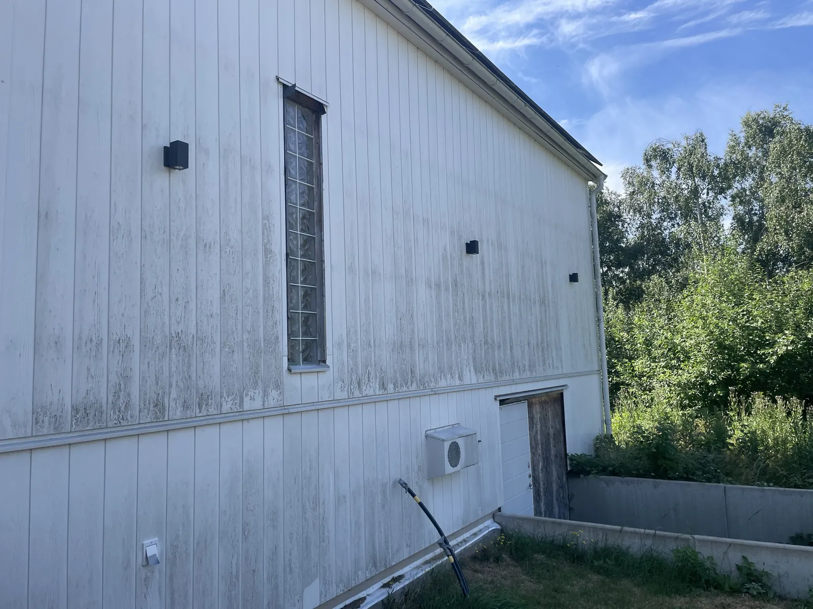 Vit träfasad med grå och grön påväxt längs panelen, särskilt på nedre delen