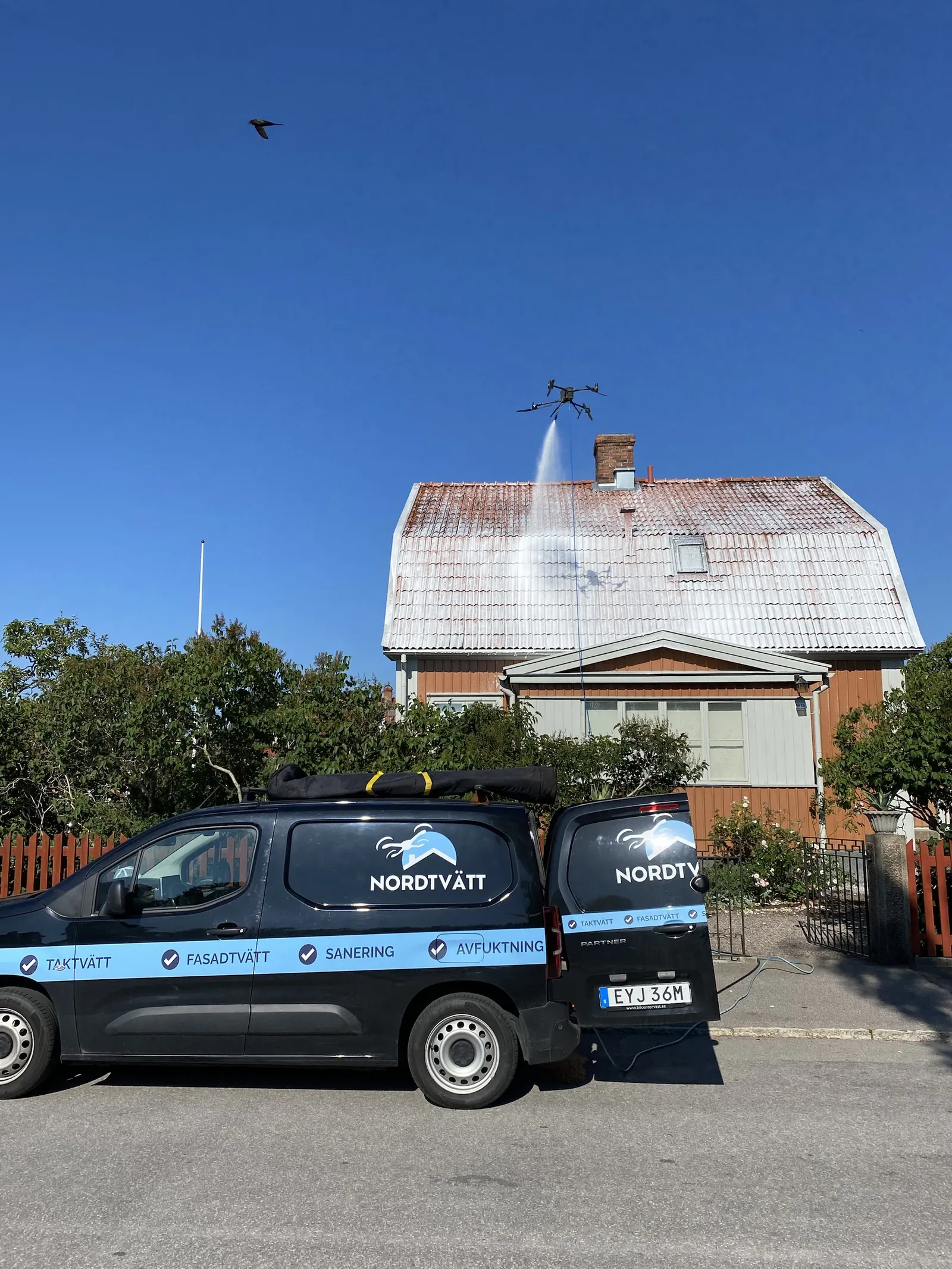 NordTvätts drönare algbehandlar ett tegeltak på en villa, med servicebilen parkerad framför